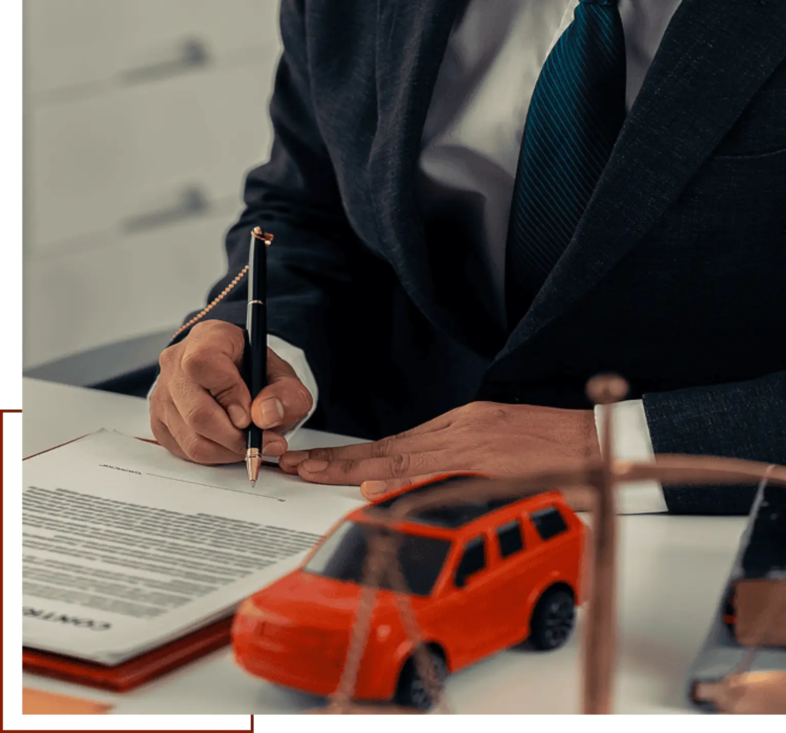 Man in a suit signing a document with a pen, while a toy car sits on the table beside him