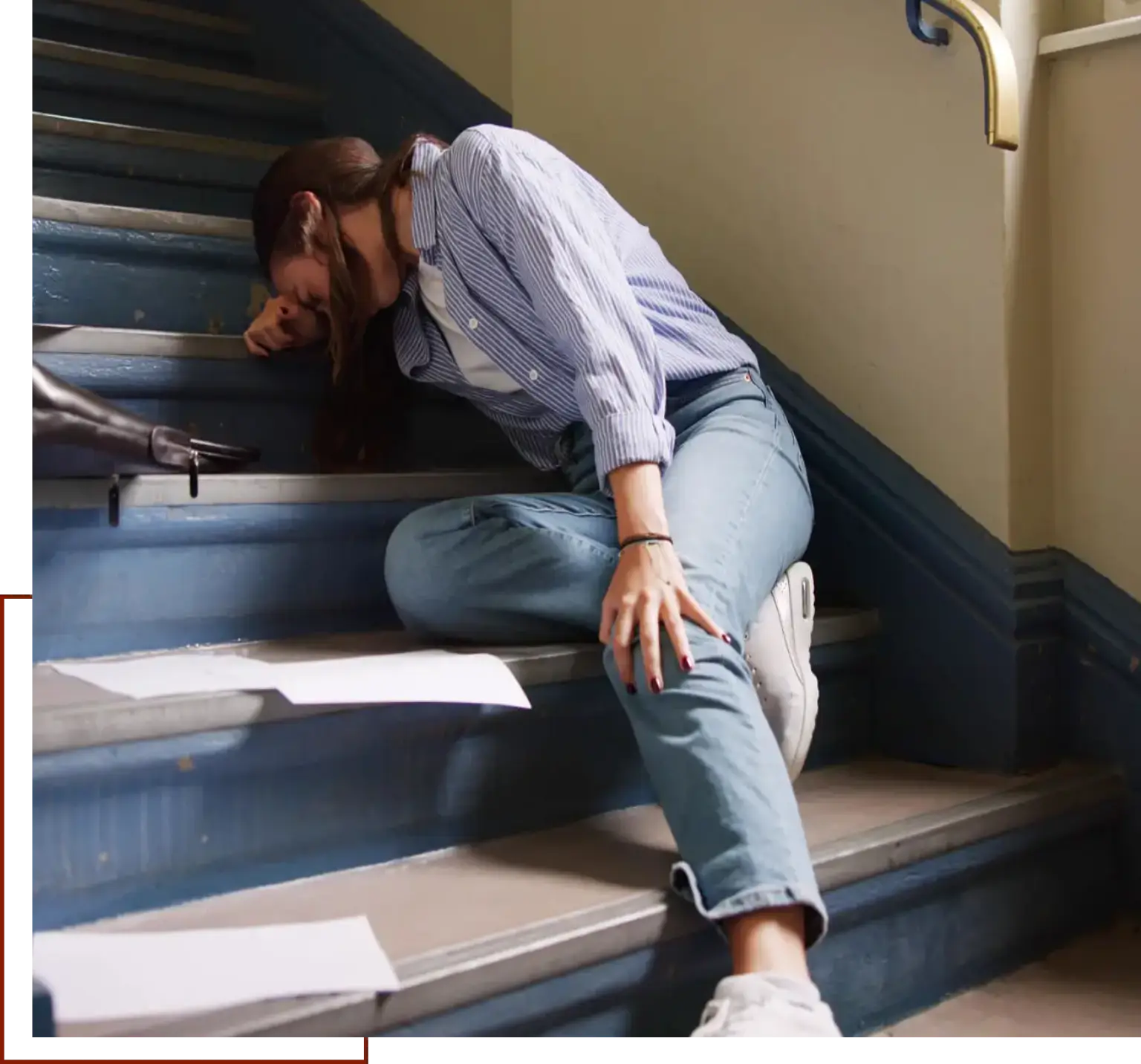 Woman sitting on the stairs with her head in her hands, surrounded by papers and a wall with a handle